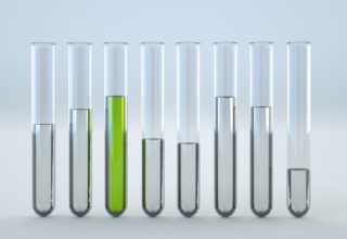 Das Bild zeigt acht Reagenzgläser, die in einer Reihe angeordnet sind. Jedes Reagenzglas enthält eine unterschiedliche Menge an Flüssigkeit. Das zweite Reagenzglas von links enthält eine grüne Flüssigkeit, während die restlichen klare Flüssigkeiten in verschiedenen Füllständen enthalten.